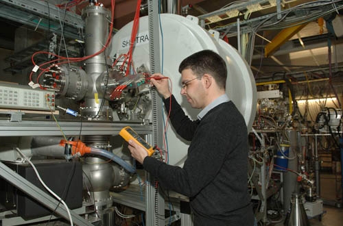 Une balance pour atomes lourds: La balance Shiptrap freine des atomes de nobelium créés artificiellement et les force à intégrer le circuit d’un piège de Penning sous l’action de champs électriques et magnétiques. Michael Block, chef de projet, vérifie les tensions aux électrodes du piège. Un aimant supraconducteur du tambour blanc crée le champ magnétique nécessaire.