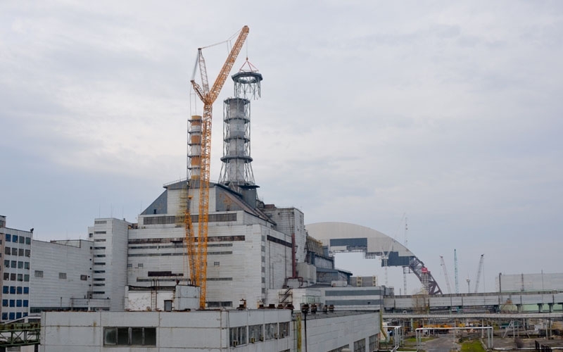 Der oberste Abschnitt des Abluftkamins wird entfernt. Nach Abschluss der Abbauarbeiten wird die neue Sicherheitshülle (gewölbte Struktur im Hintergrund) über das beschädigte Reaktorgebäude von Tschernobyl-4 geschoben.